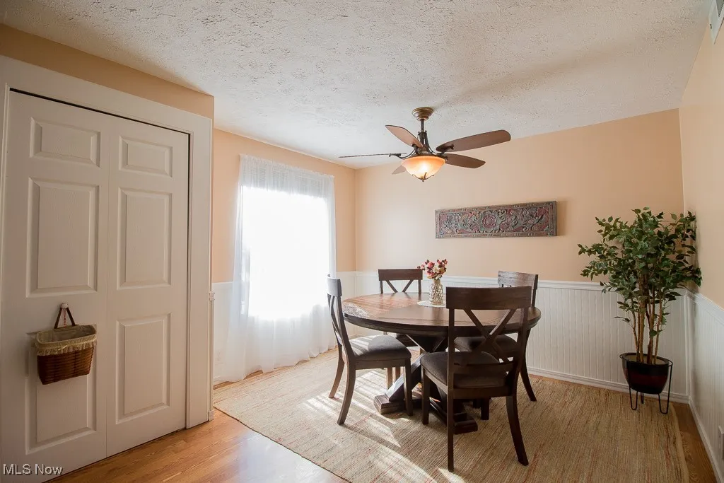 Dining area with a textured ceiling, light wood finished floors, a wainscoted wall, and ceiling fan