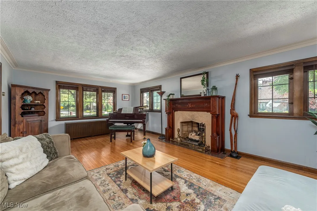 Living area with light wood finished floors, a textured ceiling, ornamental molding, radiator heating unit, and a fireplace