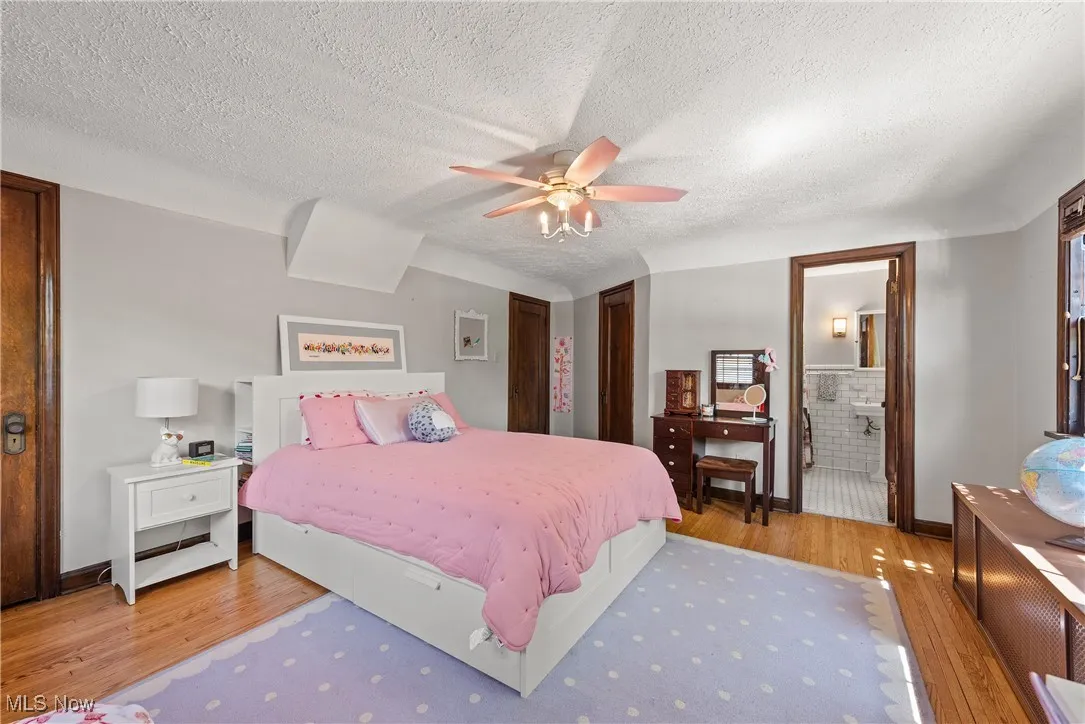 Bedroom featuring light wood finished floors, a textured ceiling, a closet, ensuite bath, and ceiling fan