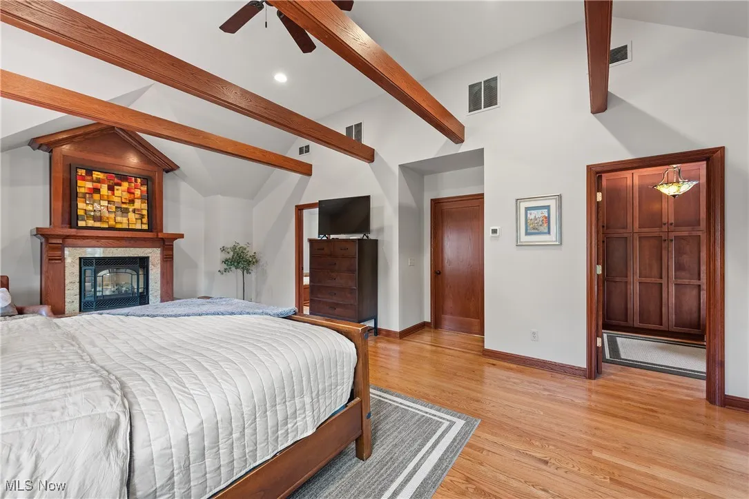 Bedroom featuring light wood-type flooring, beam ceiling, a ceiling fan, a glass covered fireplace, and recessed lighting