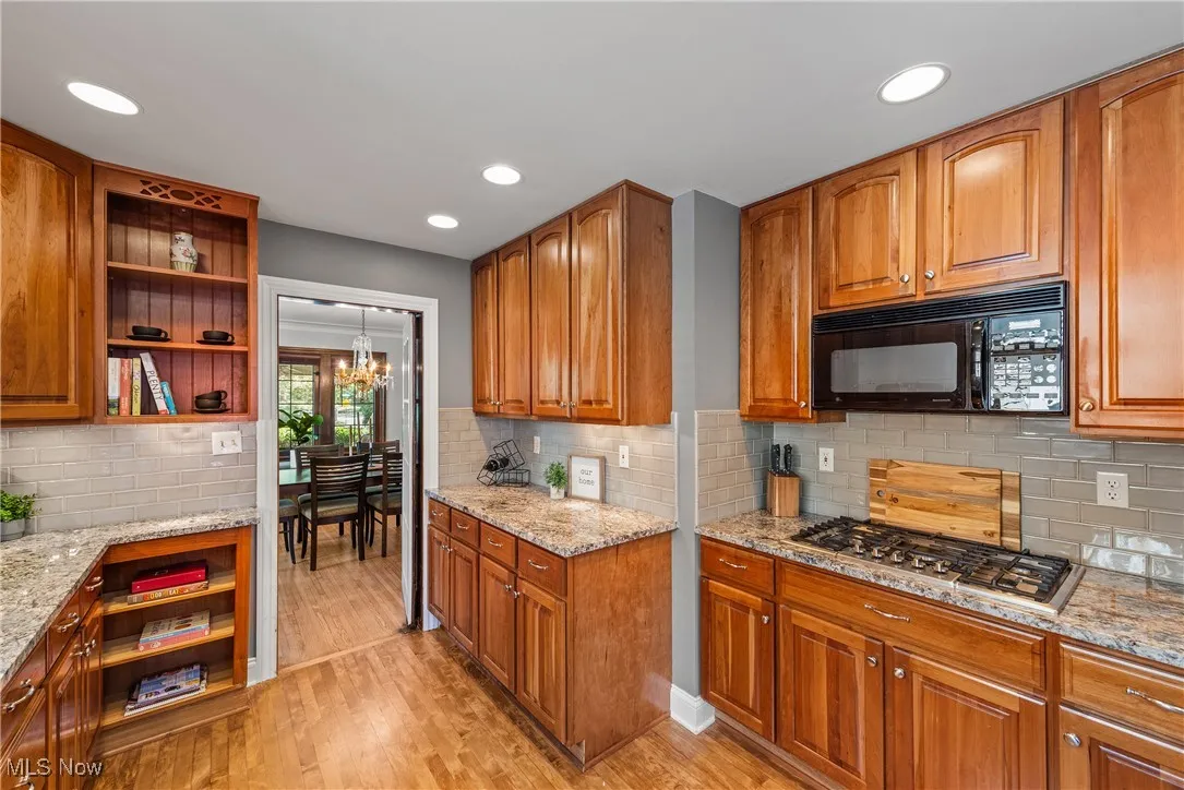 Kitchen with brown cabinets, light stone countertops, open shelves, light wood-style floors, and recessed lighting