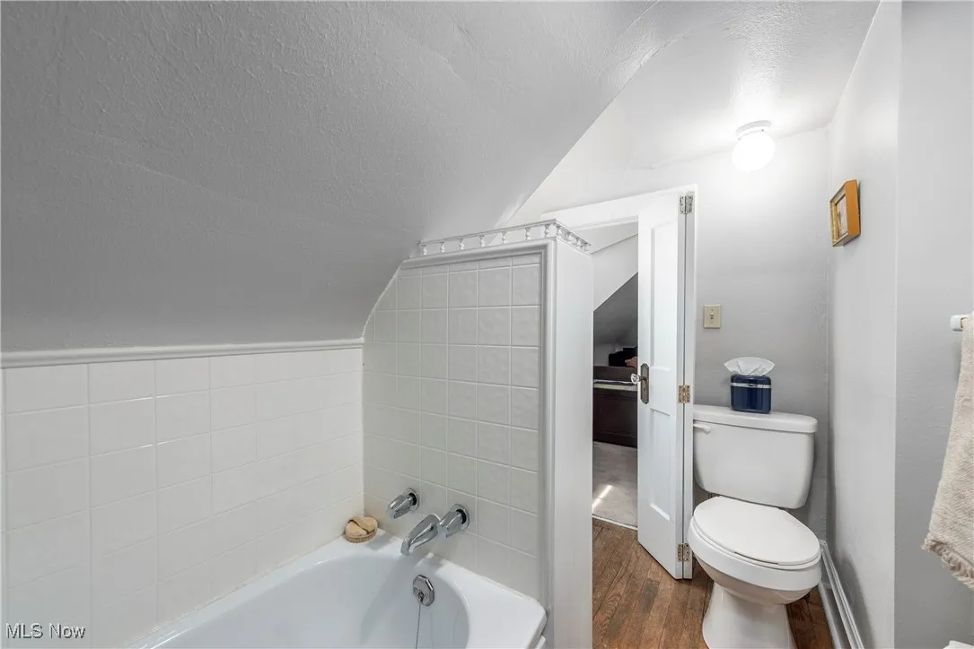 Bathroom with a textured ceiling, a bath, vaulted ceiling, and dark wood finished floors