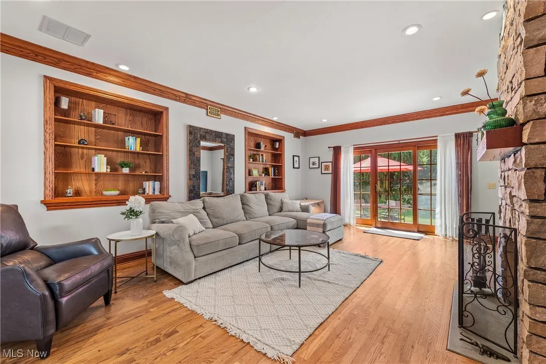 Living area featuring built in features, ornamental molding, light wood-type flooring, a stone fireplace, and recessed lighting