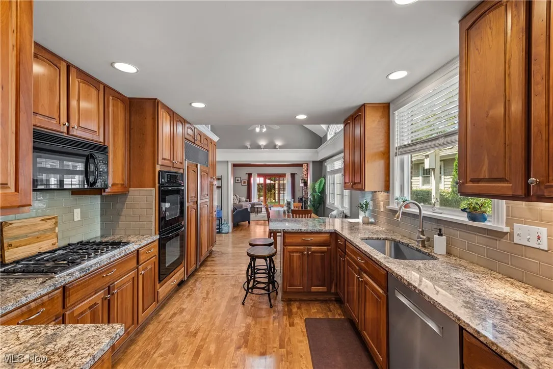 Kitchen featuring backsplash, light stone counters, a peninsula, brown cabinets, and lofted ceiling