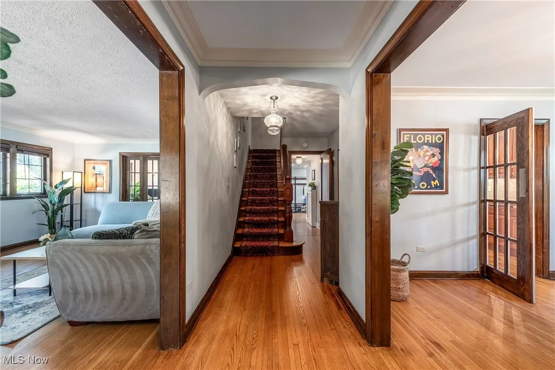 Hall with crown molding, light wood finished floors, arched walkways, stairs, and a textured ceiling