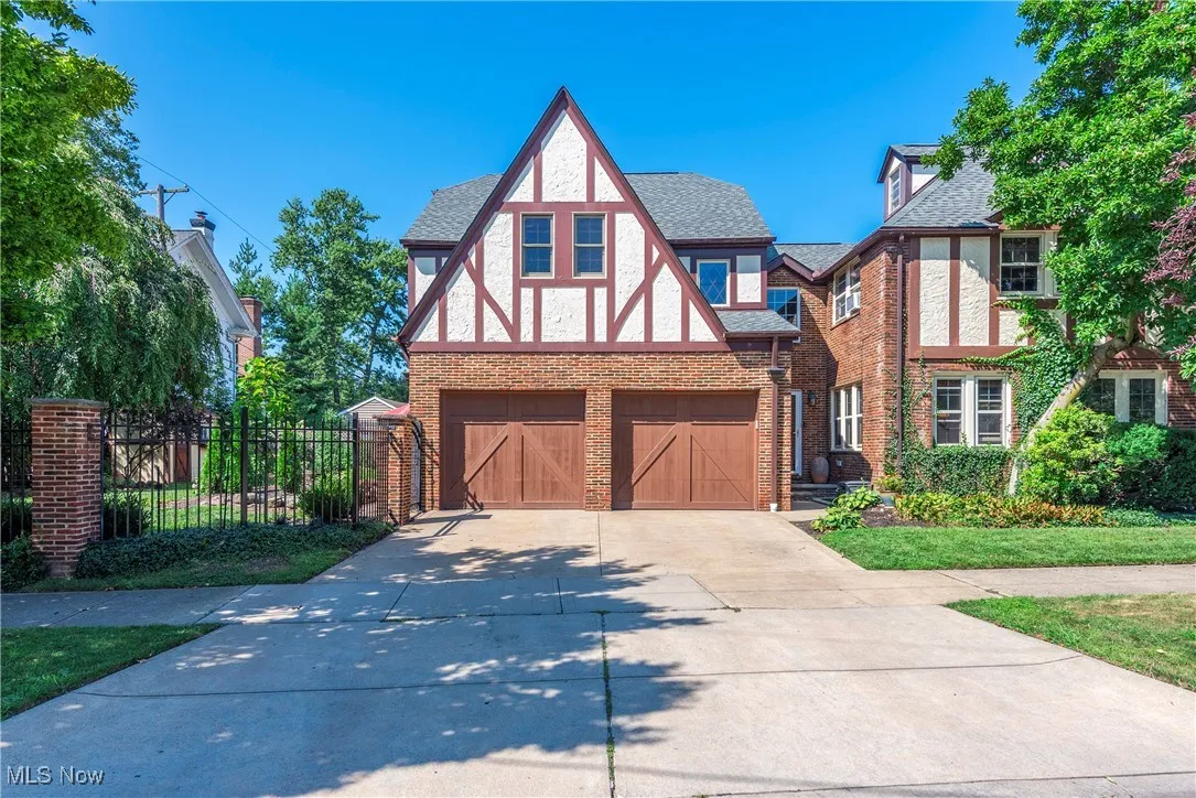 Tudor house featuring stucco siding, an attached garage, concrete driveway, brick siding, and a shingled roof