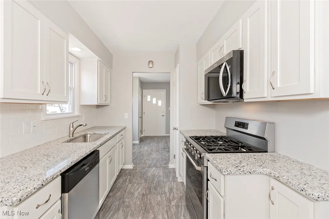 Kitchen featuring stainless steel appliances, white cabinetry, and light stone counters
