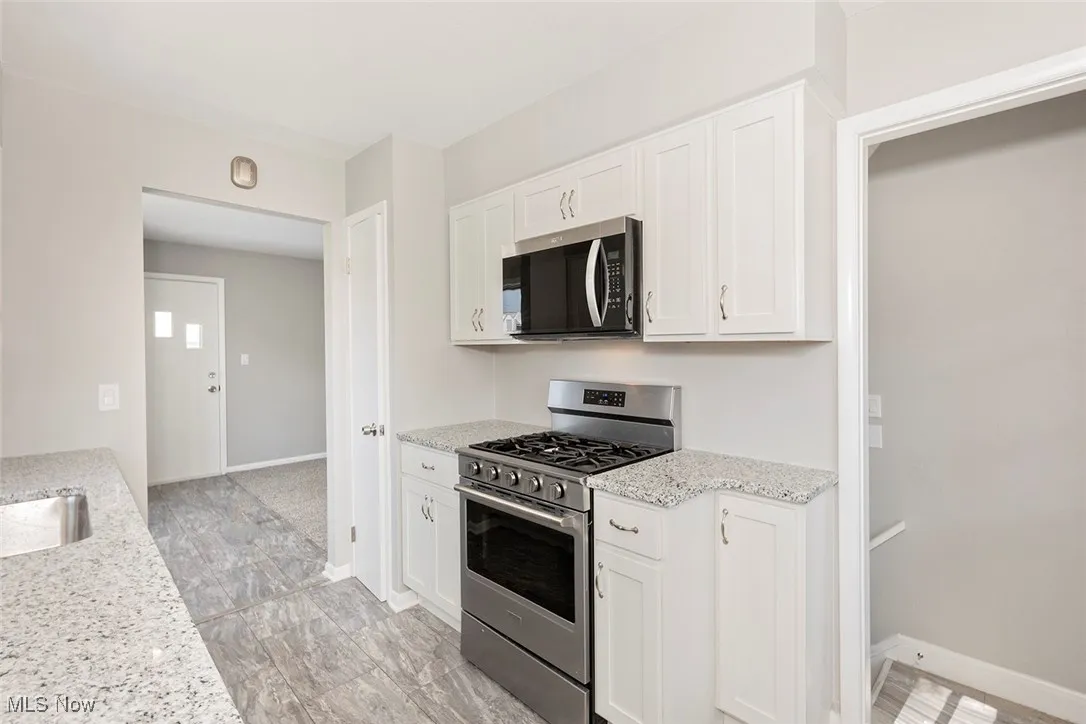 Kitchen with appliances with stainless steel finishes, white cabinets, and light stone countertops