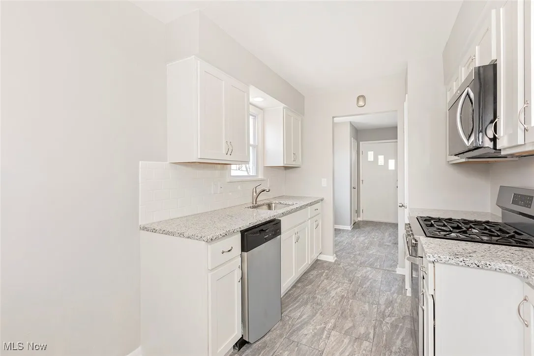 Kitchen featuring stainless steel appliances, light stone counters, and white cabinets