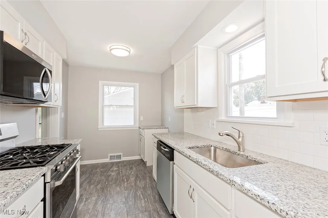 Kitchen featuring appliances with stainless steel finishes, backsplash, white cabinets, and light stone counters
