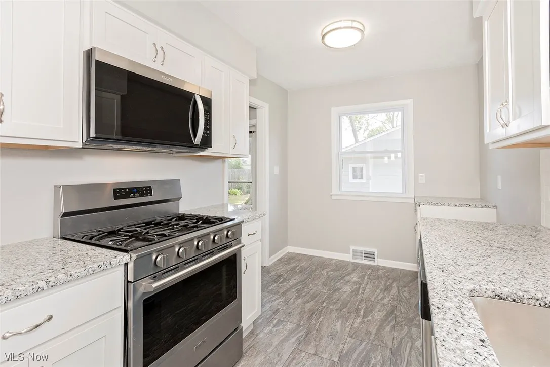 Kitchen with appliances with stainless steel finishes, white cabinets, and light stone counters