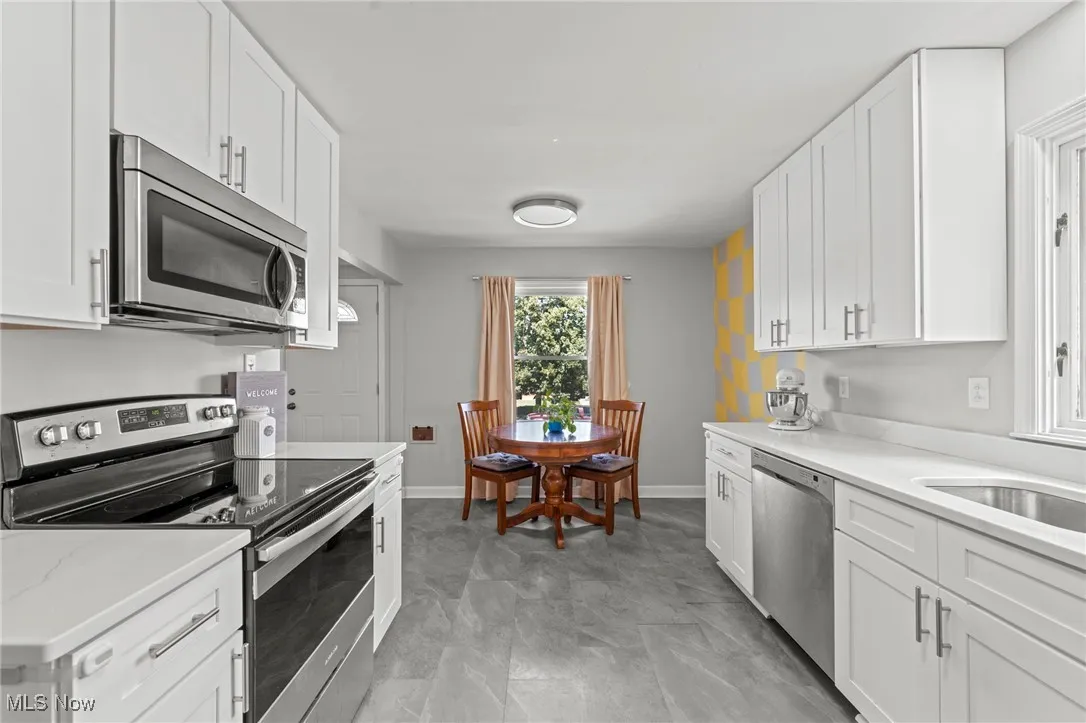 Kitchen with appliances with stainless steel finishes, white cabinets, and light stone countertops
