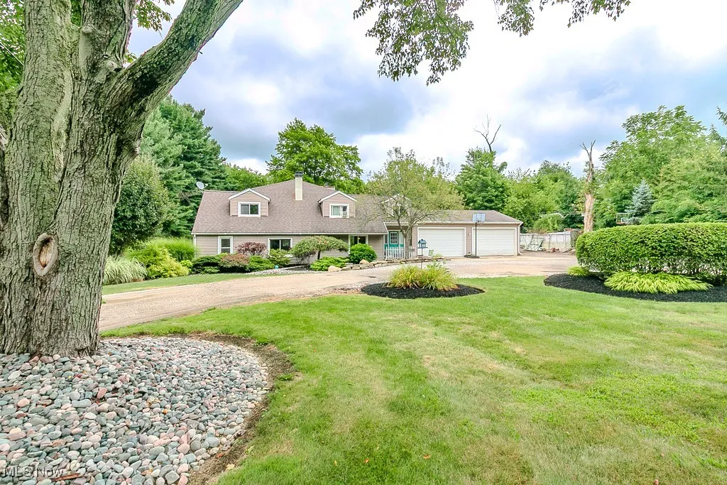 New england style home featuring dirt driveway, a front lawn, a garage, and view of scattered trees