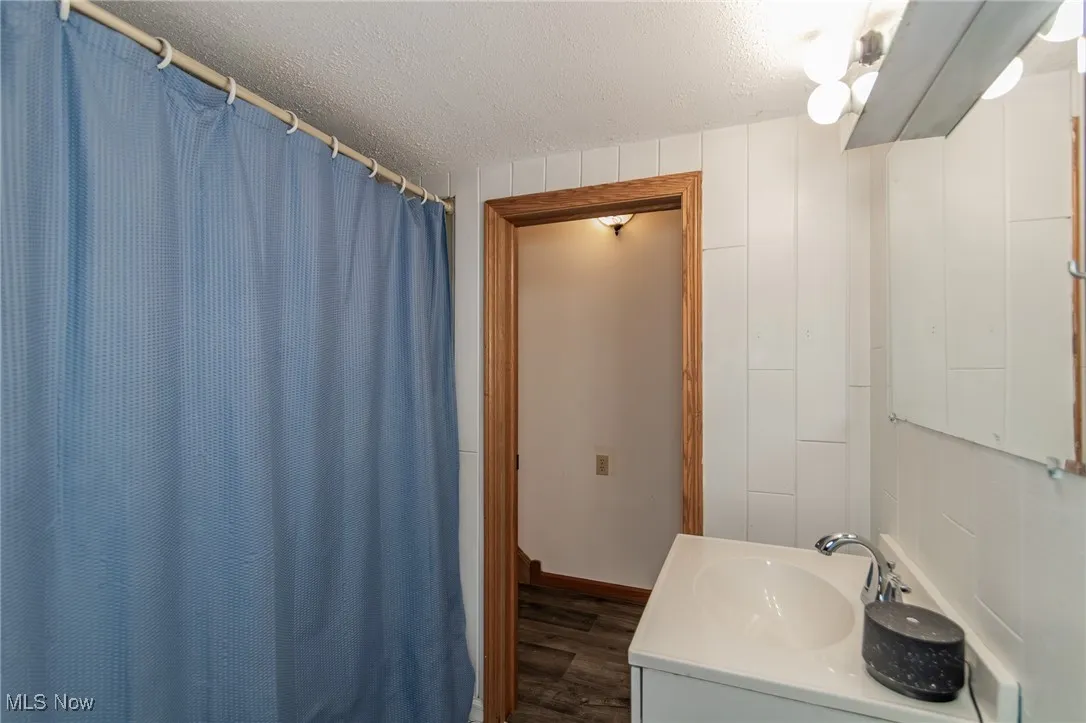 Bathroom with a textured ceiling, vanity, dark wood finished floors, and a shower with shower curtain