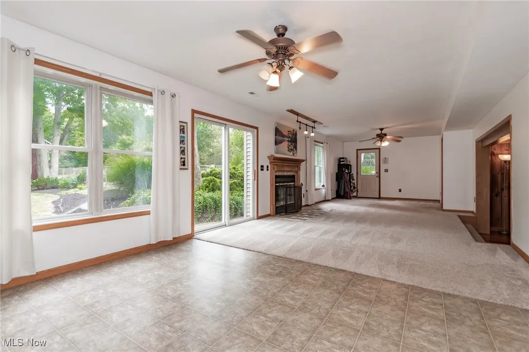 Unfurnished living room featuring a glass covered fireplace, ceiling fan, and light carpet