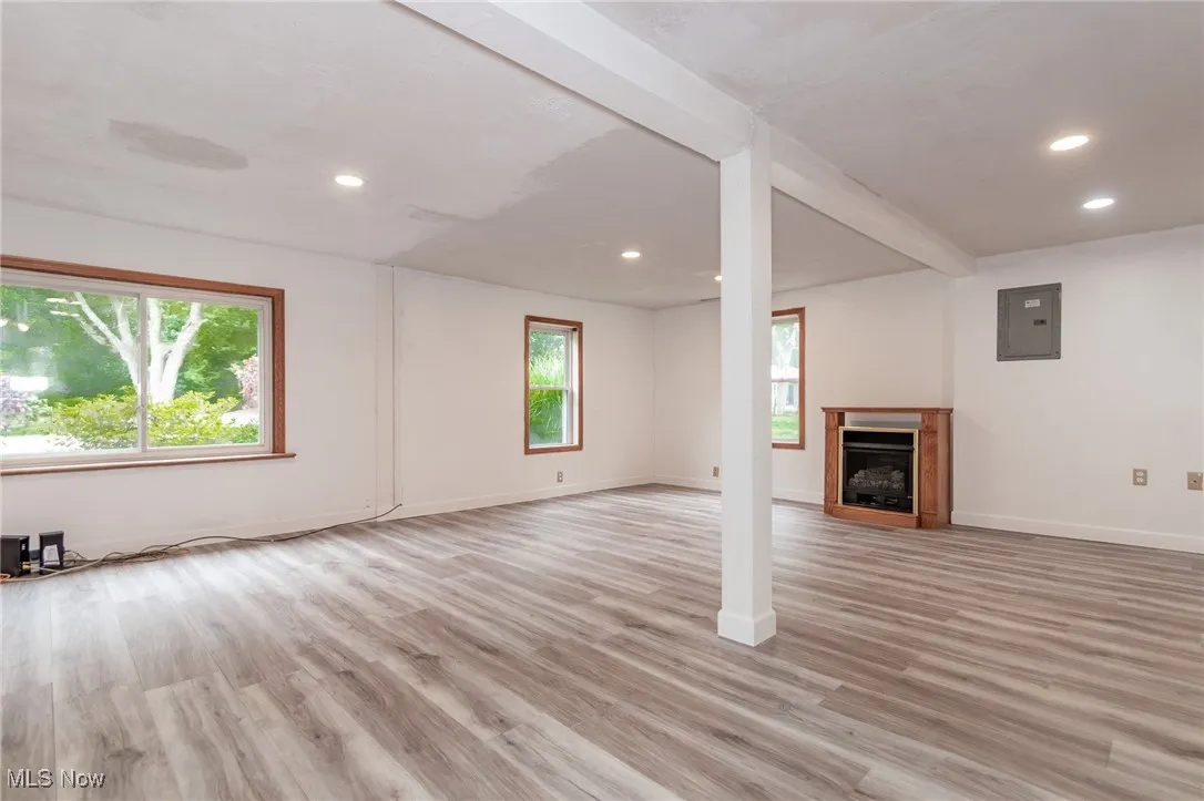 Unfurnished living room with a fireplace, light wood-type flooring, electric panel, beam ceiling, and recessed lighting