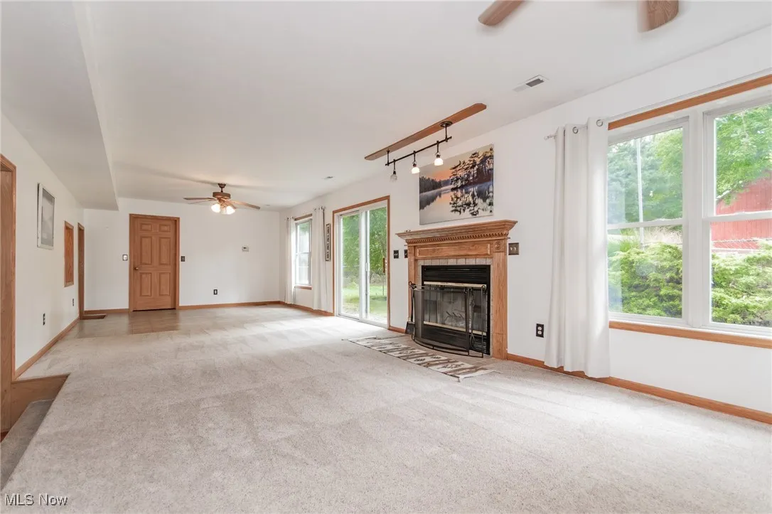 Unfurnished living room featuring a ceiling fan, light carpet, a fireplace with flush hearth, and rail lighting