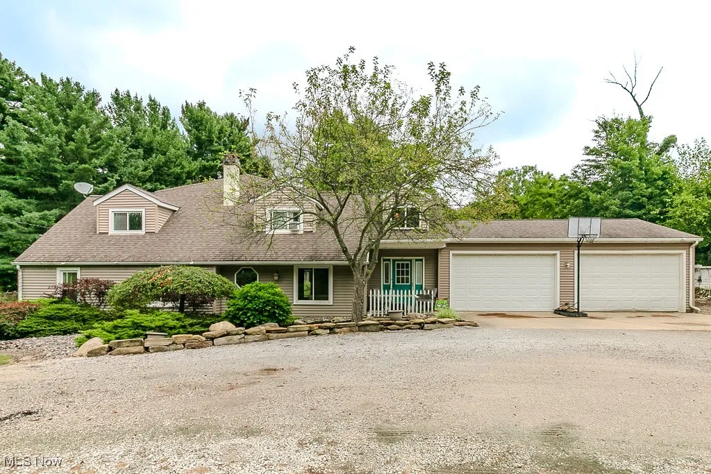 View of front of property featuring dirt driveway, an attached garage, a chimney, a porch, and roof with shingles
