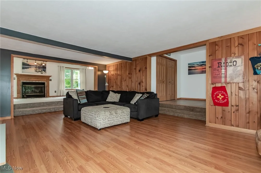 Living room featuring wooden walls, a glass covered fireplace, beam ceiling, and wood finished floors