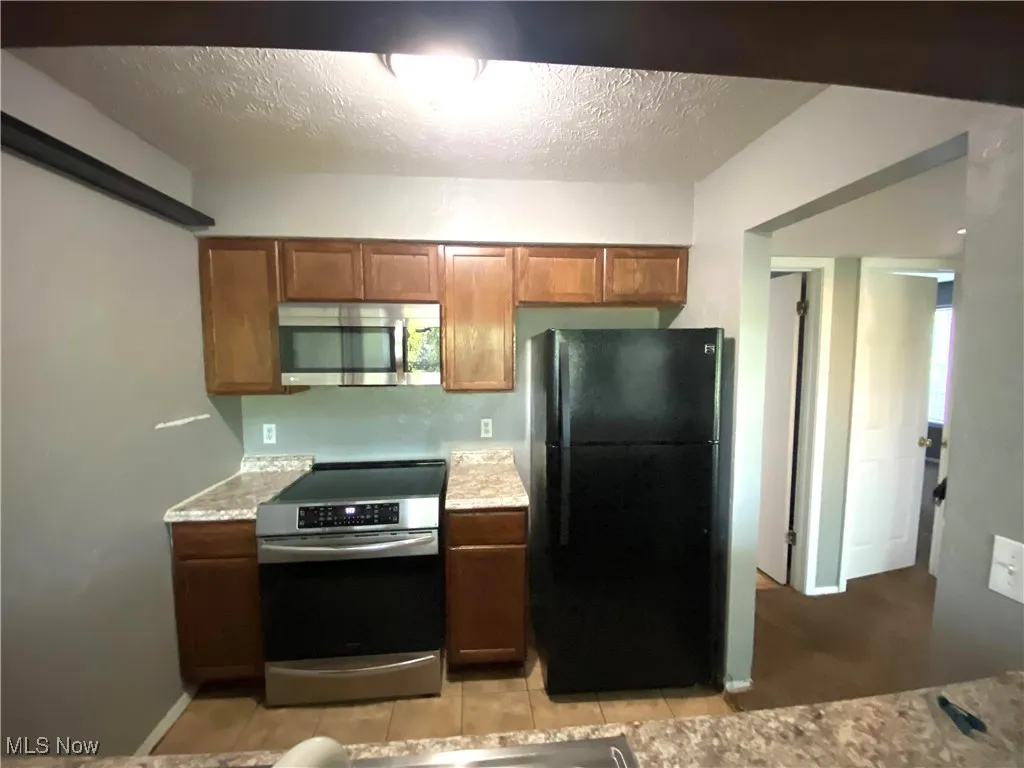 Kitchen with dark wood cabinets, laminate counters, black and stainelss steel stove and refrigerator.