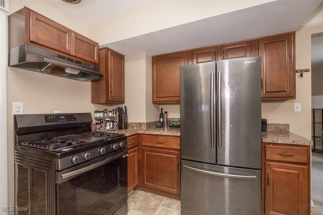 Kitchen with stainless steel appliances, under cabinet range hood, brown cabinets, and light stone counters