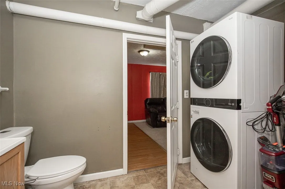 Washroom with stacked washer and clothes dryer, a textured ceiling, and light tile patterned flooring
