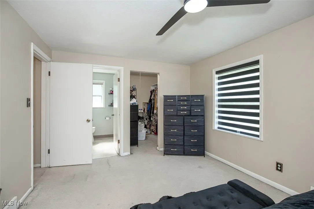 Bedroom featuring light colored carpet, a walk in closet, ensuite bath, and ceiling fan