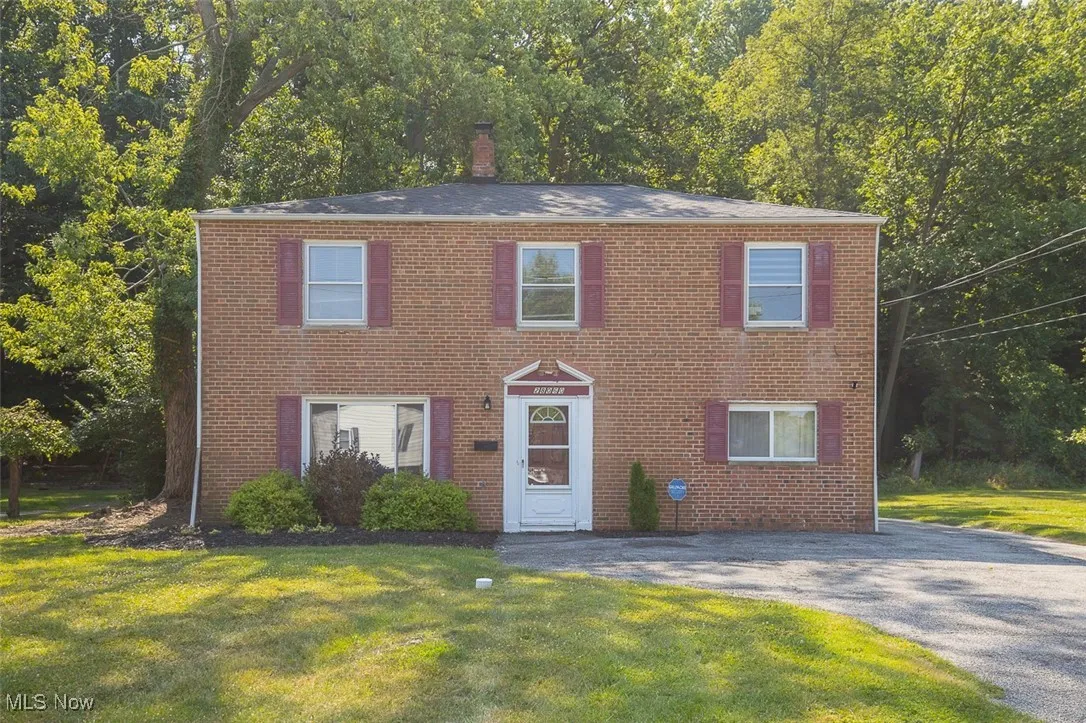 Colonial home with a front yard, a chimney, and brick siding