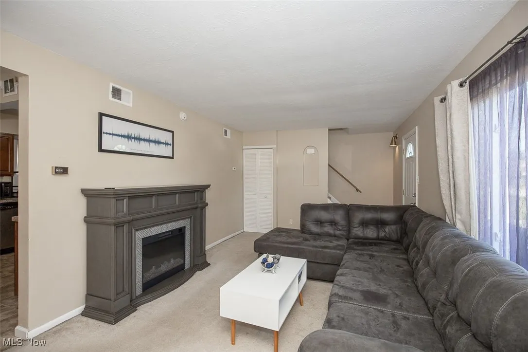 Carpeted living area with a glass covered fireplace and baseboards