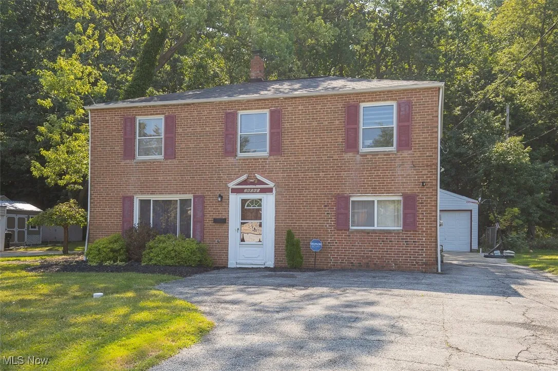 Colonial inspired home featuring brick siding, a chimney, and a garage