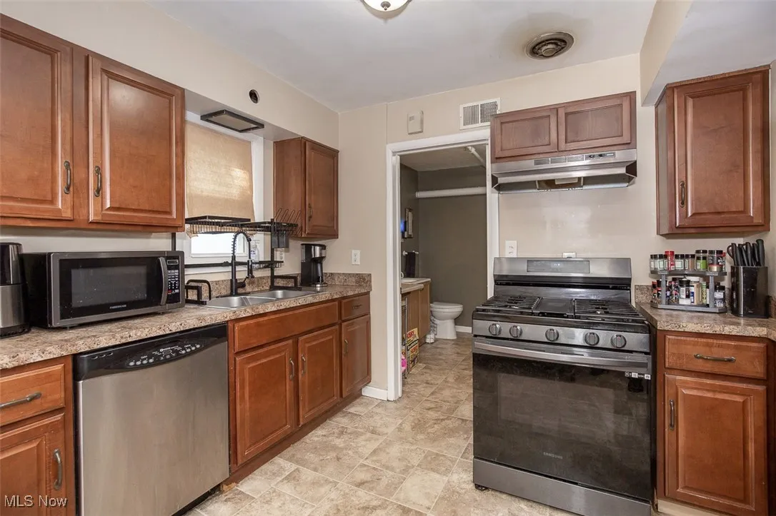 Kitchen with brown cabinets, appliances with stainless steel finishes, and under cabinet range hood