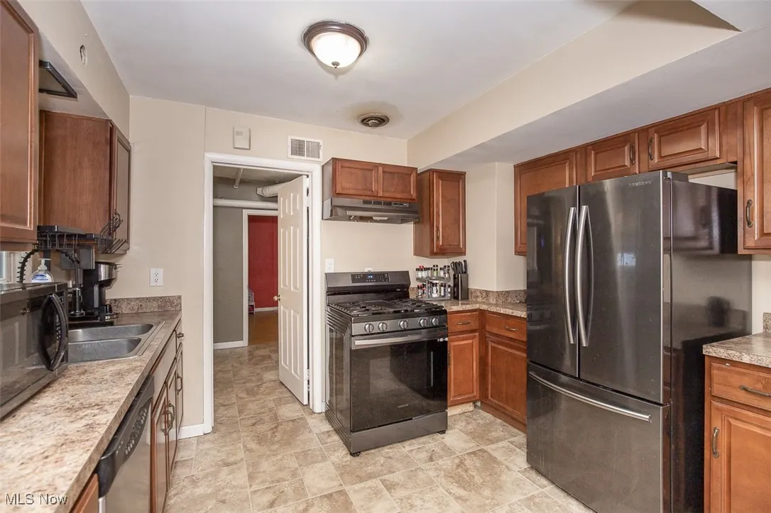 Kitchen featuring appliances with stainless steel finishes, brown cabinetry, light countertops, and under cabinet range hood