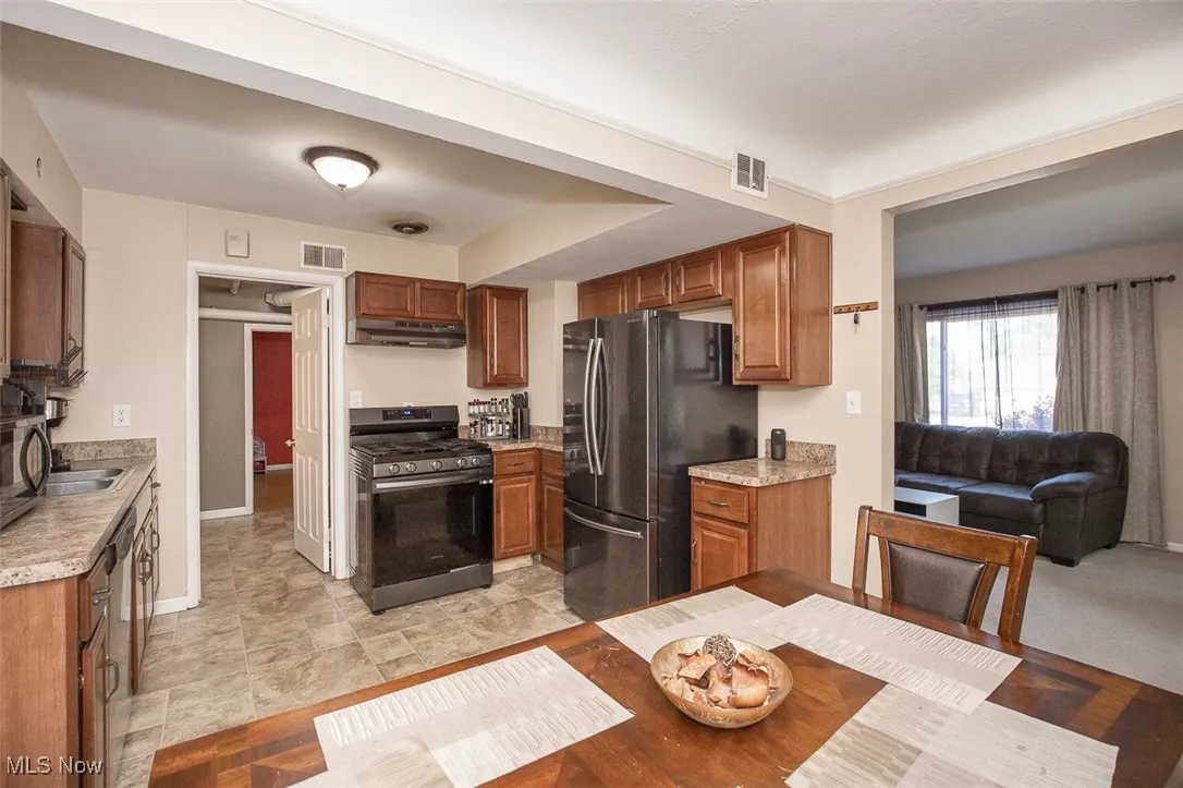 Kitchen featuring stainless steel appliances, brown cabinets, light countertops, and under cabinet range hood