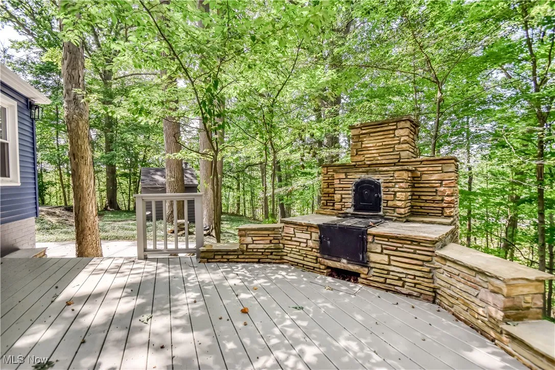 Deck featuring an outdoor stone fireplace and view of wooded area