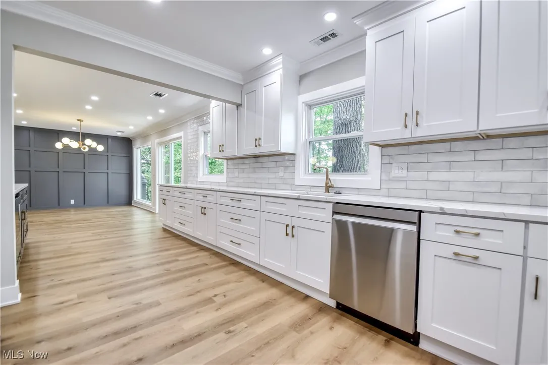 Kitchen with white cabinets, crown molding, dishwasher, light wood-style flooring, and a chandelier