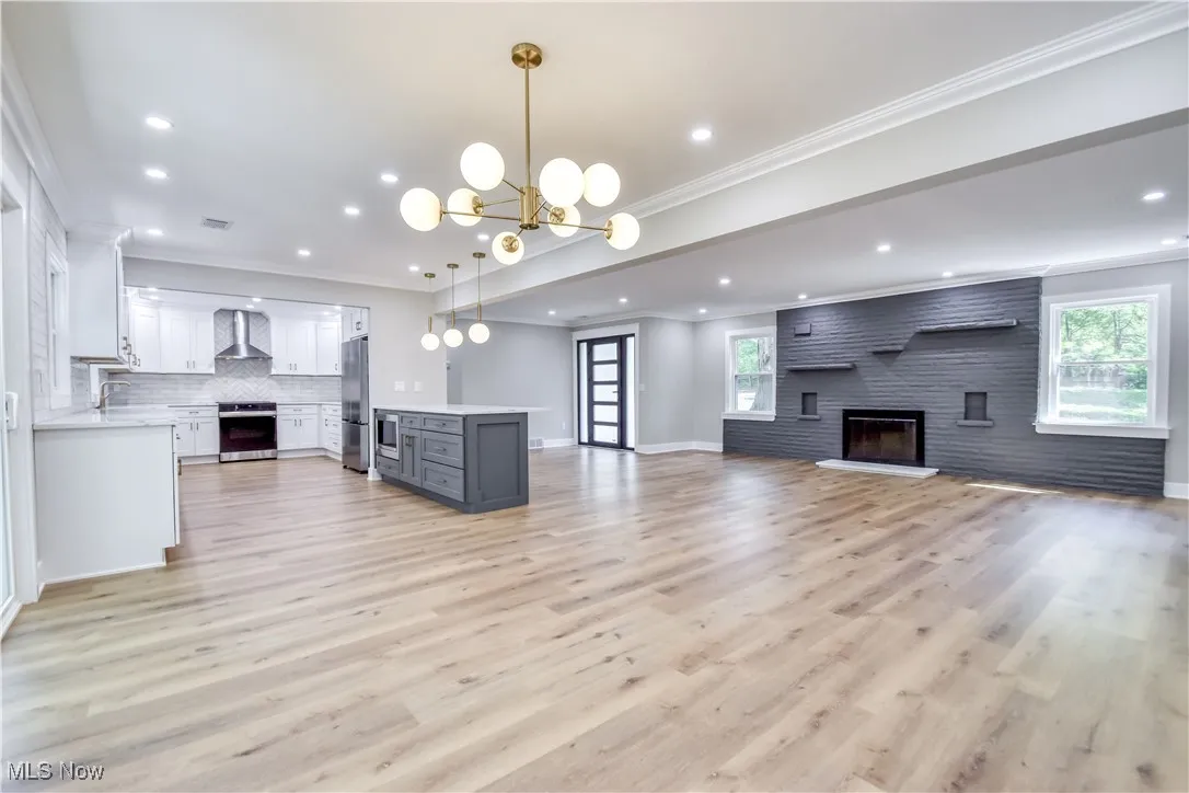 Unfurnished living room featuring a large fireplace, crown molding, light wood finished floors, a chandelier, and recessed lighting