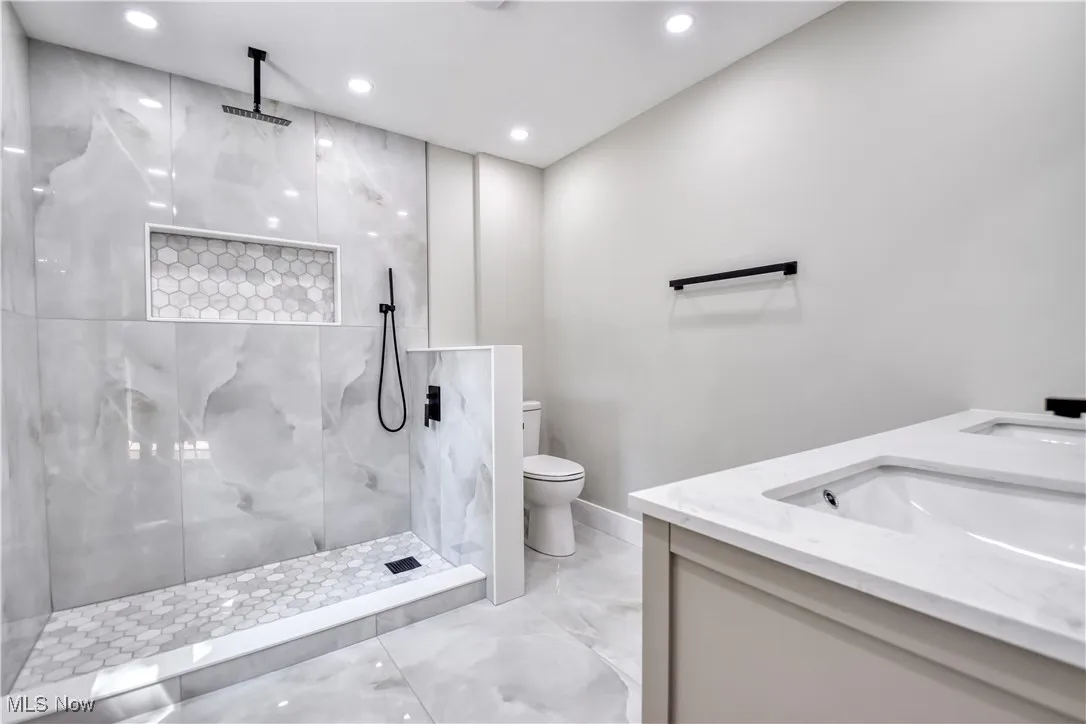 Bathroom featuring a marble finish shower, double vanity, light marble finish floors, and recessed lighting