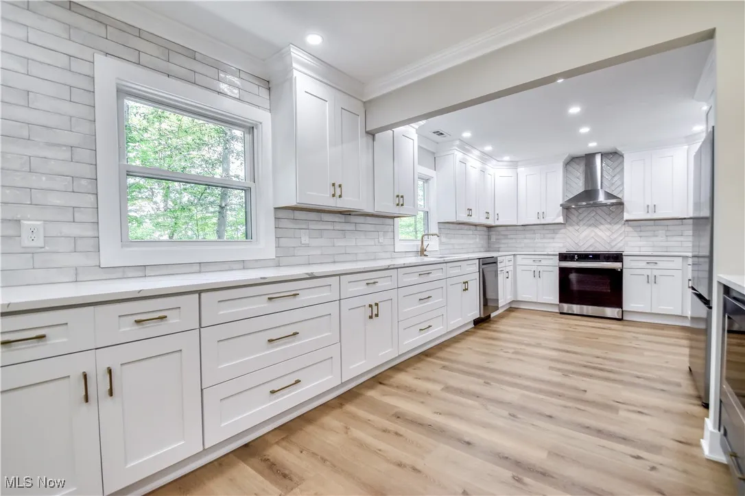 Kitchen with white cabinets, appliances with stainless steel finishes, tasteful backsplash, light wood finished floors, and light stone countertops