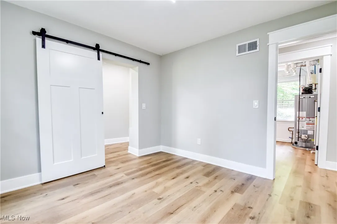 Unfurnished bedroom featuring a barn door, light wood-style flooring, and gas water heater