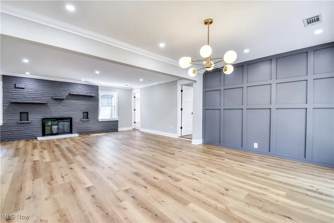 Unfurnished living room featuring light wood finished floors, ornamental molding, a fireplace, a decorative wall, and a chandelier