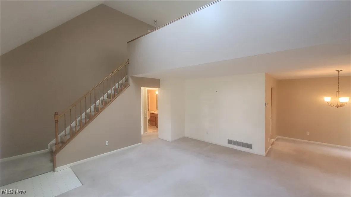 Unfurnished living room featuring carpet floors, a high ceiling, stairs, and a chandelier