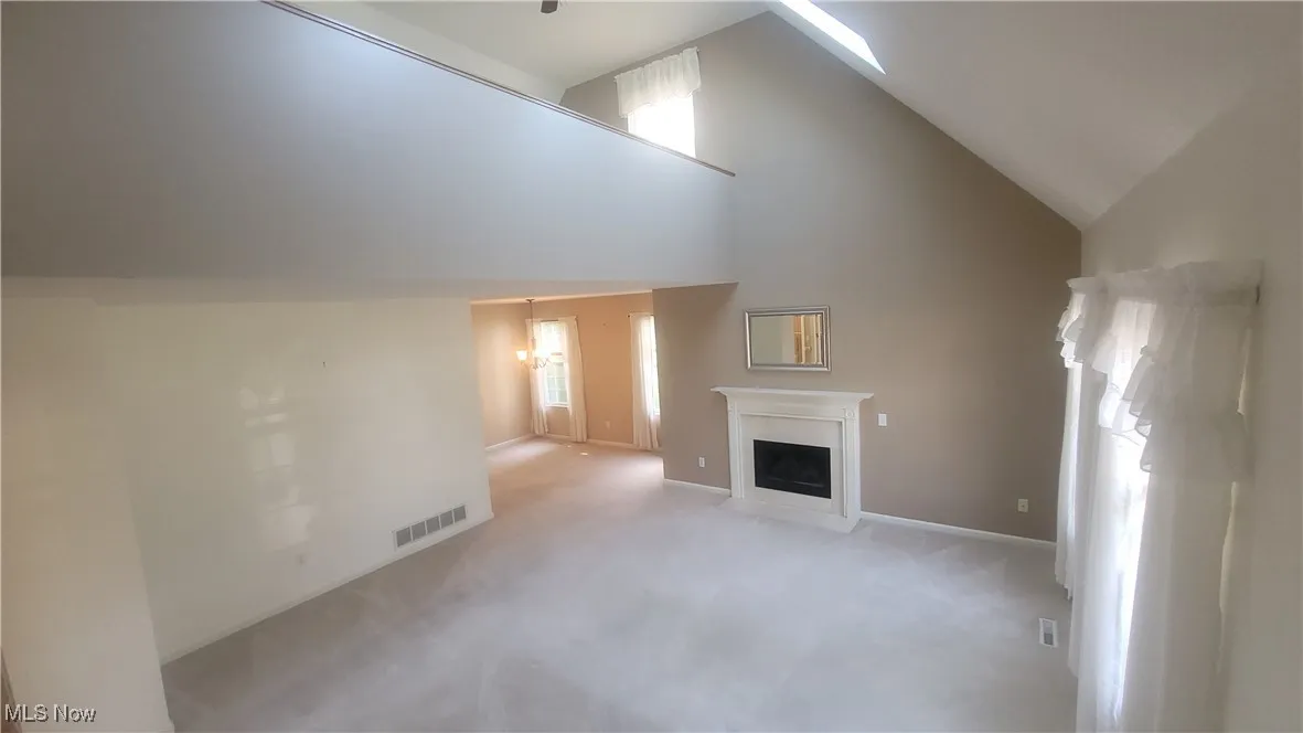 Unfurnished living room featuring carpet, a fireplace with flush hearth, and high vaulted ceiling
