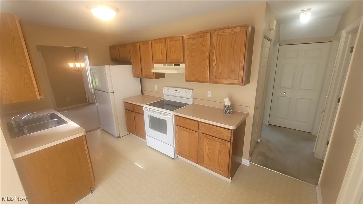 Kitchen with white appliances, light countertops, under cabinet range hood, and brown cabinets