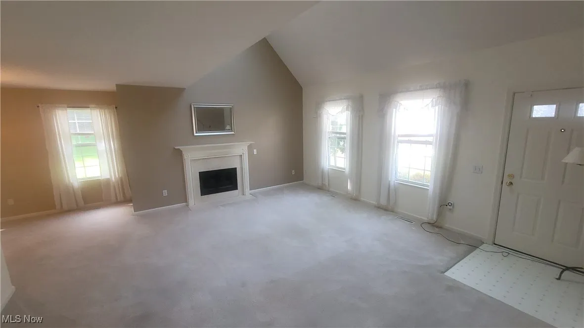 Unfurnished living room featuring carpet, a fireplace with flush hearth, and vaulted ceiling