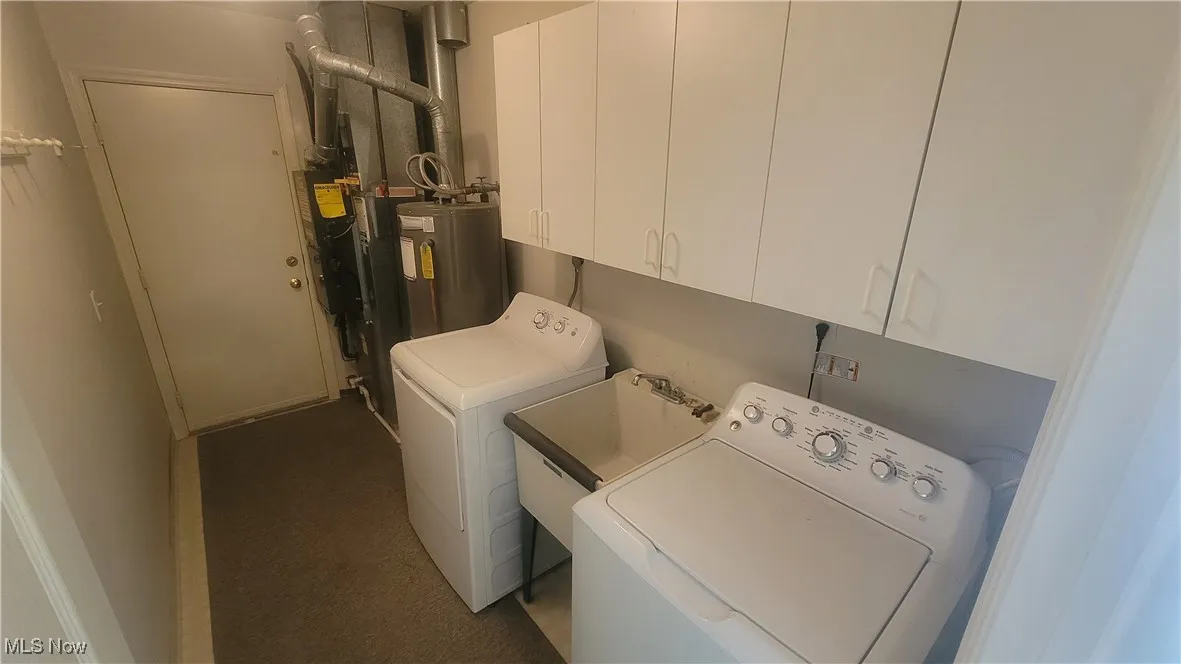 Laundry featuring cabinet space, utility tub, water heater, heating unit, and separate washer and dryer