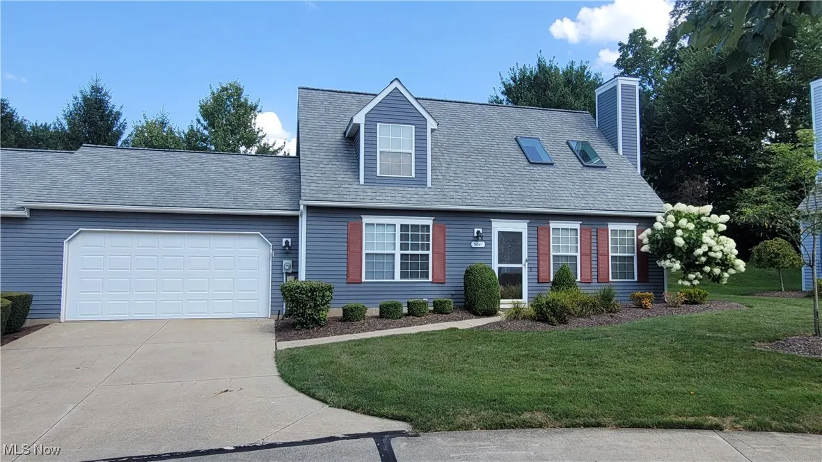 Cape cod house with concrete driveway, an attached garage, a front yard, a chimney, and roof with shingles