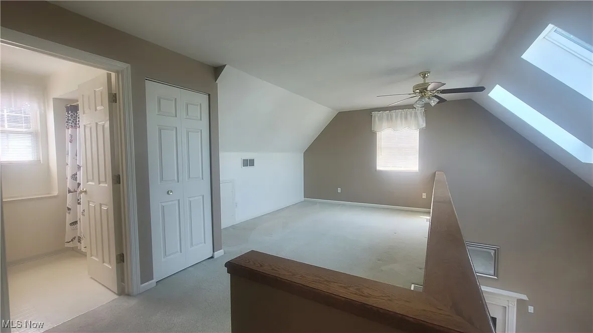 Loft with light colored carpet, a skylight, vaulted ceiling, and ceiling fan