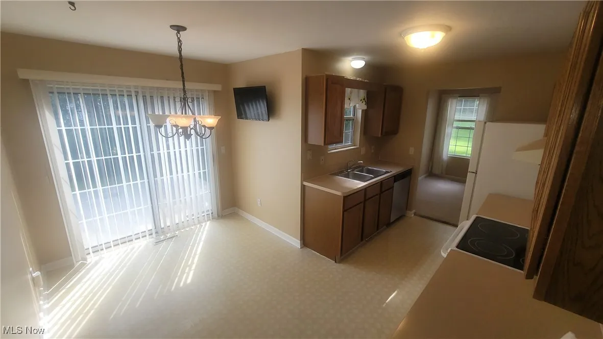 Kitchen with light countertops, a chandelier, hanging light fixtures, white appliances, and dark brown cabinetry