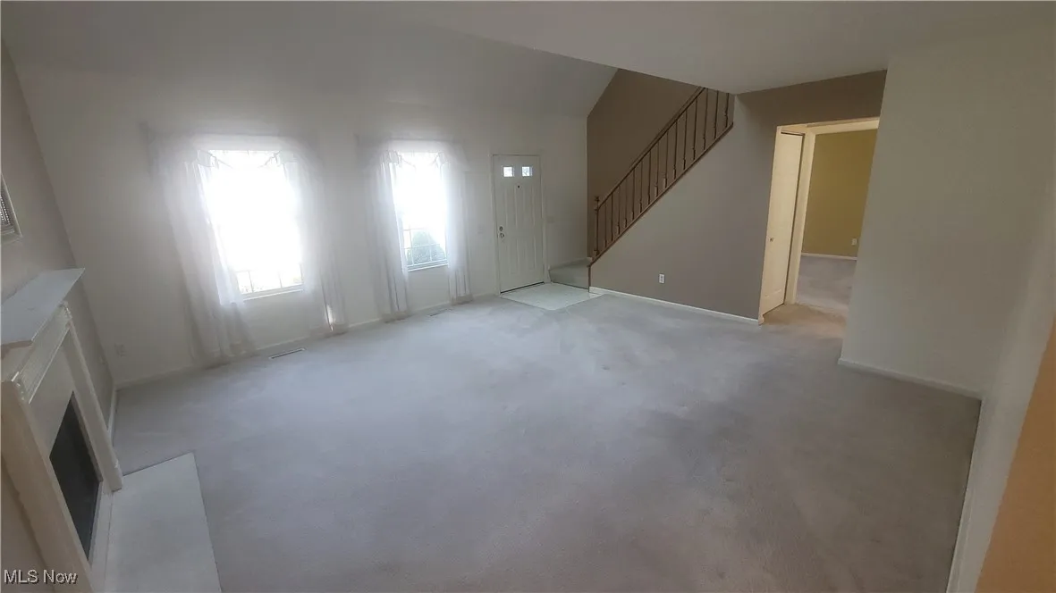Unfurnished living room featuring carpet, a fireplace, and stairway