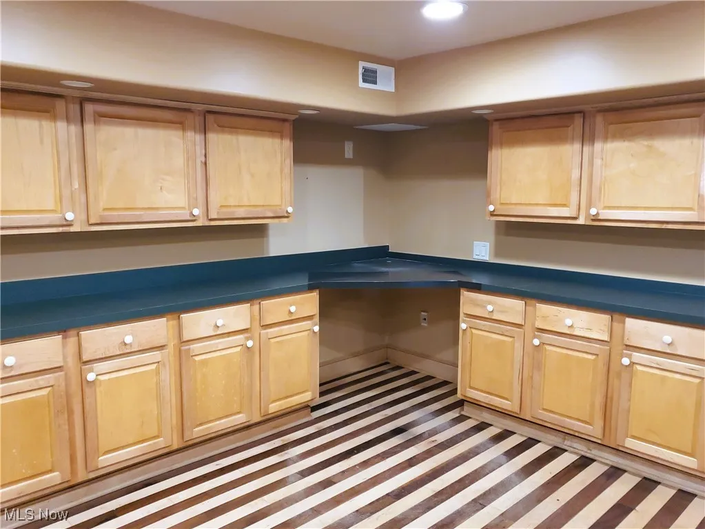 Kitchen featuring dark countertops, inlaid floor details, recessed lighting, light brown cabinets, and built in desk